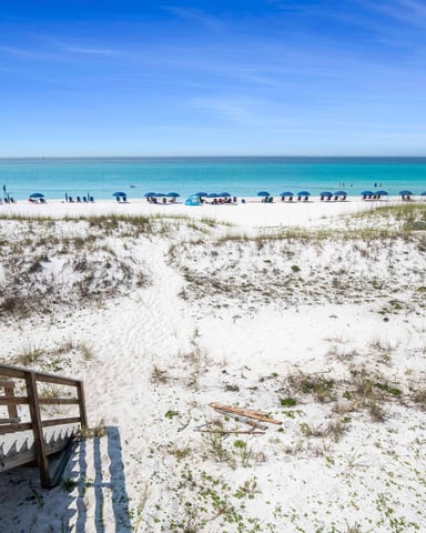 Beach access boardwalk steps leading to white sand and turquoise Gulf water