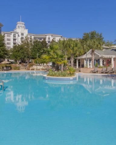 Large resort pool with palm trees, white buildings with cupolas, and lounge chairs under clear blue sky