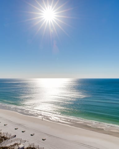 Sunny beach with white sand, turquoise water, and lounge chairs along the shore