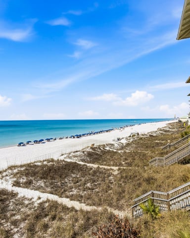 White beachfront house with multi-level decks overlooking sandy beach, dunes, and turquoise ocean water