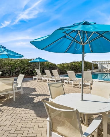 Poolside patio with turquoise umbrellas, lounge chairs, and swimming pool under clear blue sky