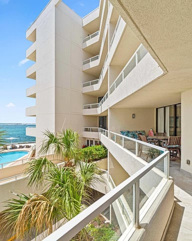 Beachfront apartment balcony with ocean and pool views, palm plants, and modern high-rise building