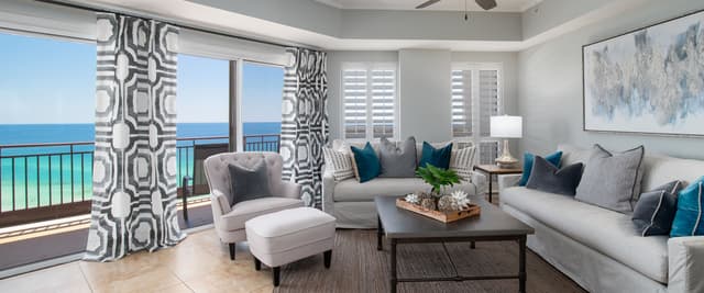 Beachfront living room with gray sofas, teal pillows, ocean view balcony, and geometric patterned curtains