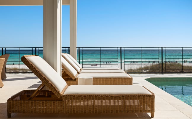 Wicker lounge chairs beside a private pool with the Gulf of Mexico in the background