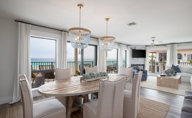 Open-plan dining and living room with ocean view, beaded chandeliers, and coastal furnishings