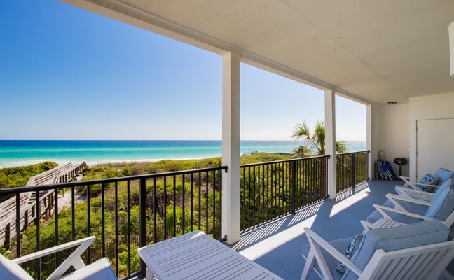 Beachfront deck with lounge chairs overlooking turquoise ocean, white sand beach, and coastal vegetation