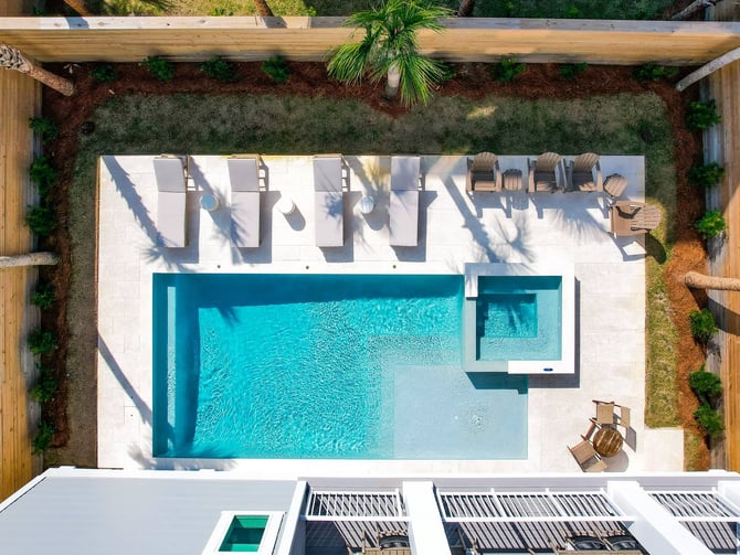 Overhead view of modern backyard with rectangular turquoise pool, white deck, lounge chairs, and wooden pergola with tropical plants