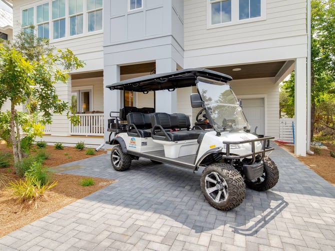White golf cart parked under carport of modern two-story beach house with white siding and large windows