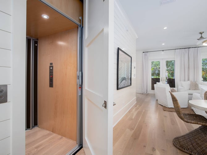 Elevator with wood interior opening to modern living room with white furniture and glass doors to outdoor patio