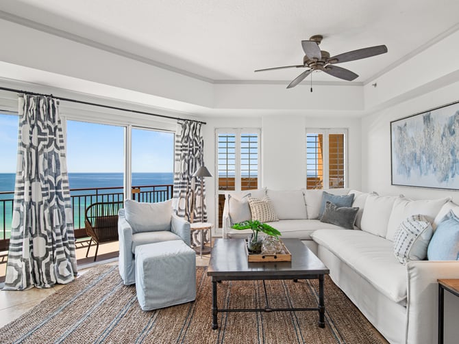 Bright beachfront living room with ocean view, white sectional sofa, patterned curtains, and balcony access